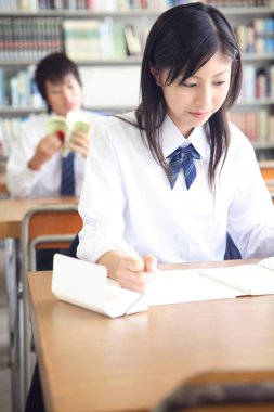 Genç Japon liseli kız kütüphanede okuyor.