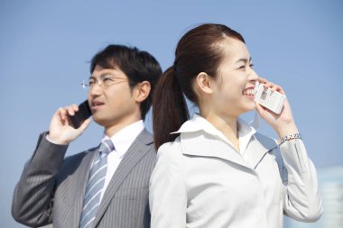 Bir adam ve bir kadın iş kıyafetleri içinde cep telefonuyla konuşuyor.