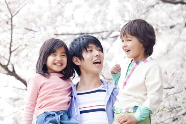 Arka planda çiçek açan kiraz ağacı olan mutlu Asyalı bir aile.