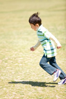 Küçük çocuk yeşil alanda futbol oynuyor.