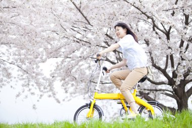 Mutlu Japon kadın bahar parkında sarı bisiklet sürüyor.