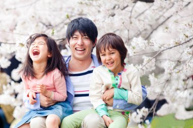 Çiçek açan kiraz ağacıyla üç kişilik Asyalı genç bir aile.
