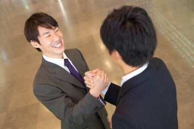 Takım elbiseli iki adam lobide el sıkışıyor.