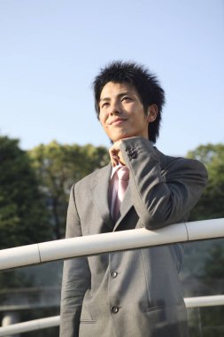 Takım elbiseli ve kravatlı bir adam korkuluklara yaslanıyor.