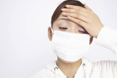 Yüz maskesi takan genç Asyalı kadının beyaz arka planda izole edilmiş baş ağrısı var. 