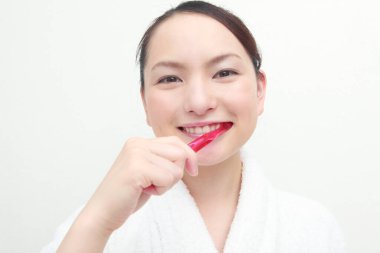 Güzel Asyalı genç kadın dişlerini fırçalıyor, beyaz arkaplan.