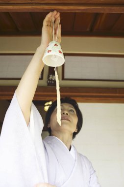 Kimonolu olgun Asyalı kadın rüzgar çanı tutuyor.