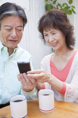 Olgun Asyalı çift telefon kullanırken kahve ya da çay içiyor. 