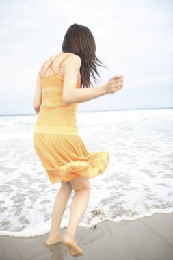 Plajda yürüyen elbiseli genç bir kadın.