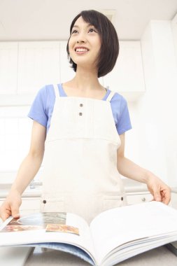 Mutfakta yemek tarifi kitabı okuyan genç bir kadın.