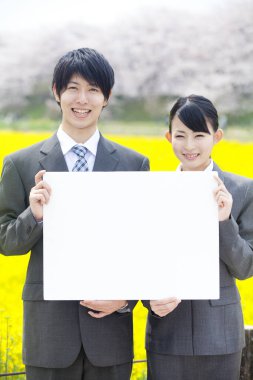 Japon iş ortaklarının portresi. Sarı çiçek tarlasının önünde boş pankart tutuyorlar.