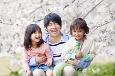 Arka planda çiçek açan kiraz ağacı olan mutlu Asyalı bir aile.