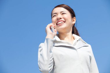 Arka planda mavi gökyüzü olan bir kadın cep telefonuyla konuşuyor.