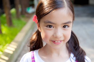 Asyalı küçük kız dışarıda gülümsüyor. 