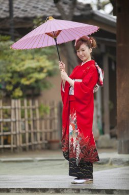 Kırmızı kimonolu, şemsiyeli güzel Asyalı kadın.