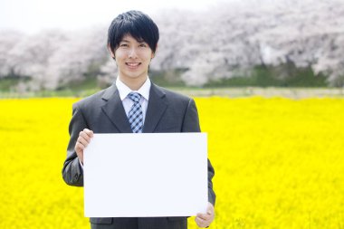 Asyalı işadamı elinde beyaz boş bir ilan panosu tutuyor.