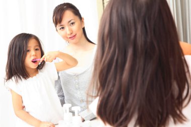 Kadın ve kız banyo aynasında dişlerini fırçalıyorlar.