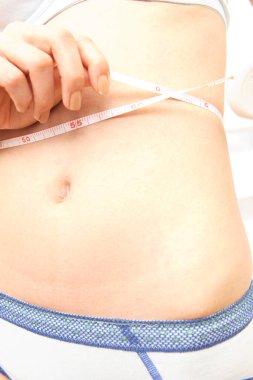 Genç bir kadın göbeğini bir mezura ile ölçüyor. Kilo kaybı ve sağlıklı yaşam kavramı