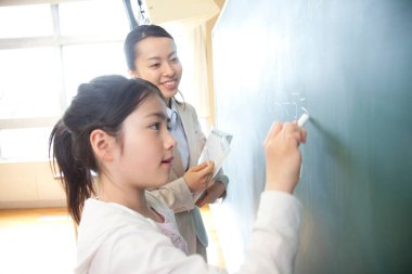 Japon liseli kız ve öğretmen okulda tahtada alıştırma yapıyorlar.