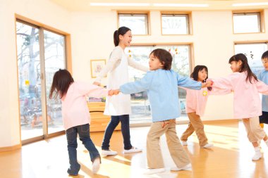 Anaokulunda Asyalı çocuklar dans edip öğretmenleriyle el ele tutuşuyorlar.. 