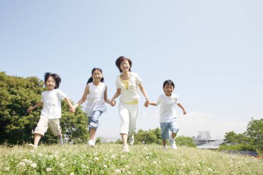 Parkta koşan dört kişilik mutlu bir ailenin portresi. Çocuklu bir anne çocuklarla el ele tutuşuyor.