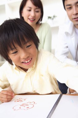 Albümde resim yapan genç Asyalı çocuk, arka planda gülümseyen ebeveynler. 