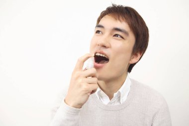 Asyalı bir adam spreyle dişlerini temizliyor.