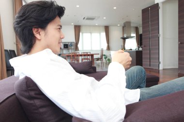 Kanepede oturan bir adam elinde kupa tutuyor.