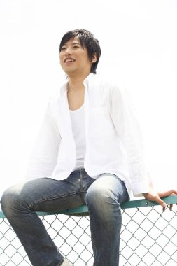 Bir adam dışarıda çitin üzerinde oturuyor.