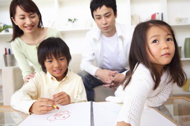 Albümde resim yapan Asyalı çocuklar, arka planda gülümseyen aileler. 