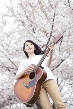 Genç Asyalı kadın bahar bahçesinde gitarla poz veriyor..