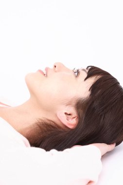 Genç bir kadın beyaz bir odada yatakta yatıyor.