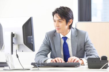 Elinde klavye ve monitörle masada oturan takım elbiseli bir adam.