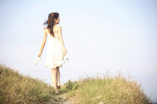 Young woman in white dress walking on the grass barefoot
