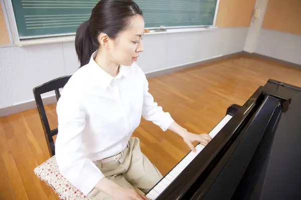 Genç Asyalı kadın öğretmen piyano çalıyor.
