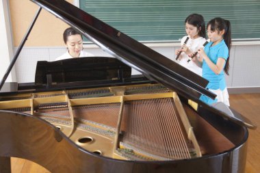 Asyalı kızlar öğretmenleri müzik dersi sırasında piyano çalarken flüt çalarlar.