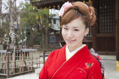 Geleneksel kırmızı kimonolu güzel gülümseyen Japon kadın tapınağı ziyaret ediyor.