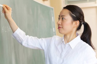 Sınıf dersi sırasında tahtada tebeşirle Asyalı öğretmen  