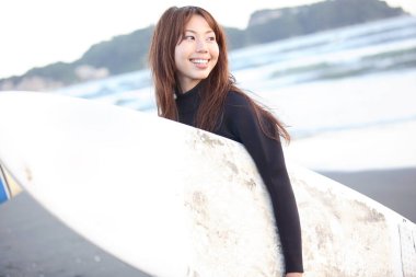 Deniz kıyısında sörf tahtası olan Asyalı genç bir kadın.