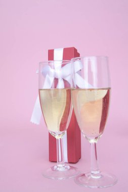 Hediye kutusu ve pembe arka planda şarap kadehleri    