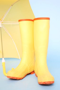 Mavi arka planda sarı lastik çizmeler ve şemsiye