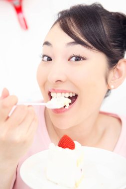 Asyalı kadın çilekli pasta yiyor. 