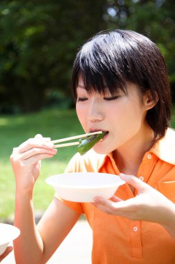 Asyalı kadın dışarıda çubuklarla yemek yiyor.