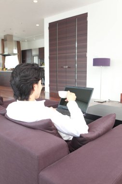 Kanepede dizüstü bilgisayarlı bir adam oturuyor.