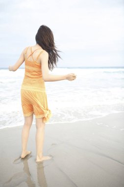 Genç bir kadın sahilde yürüyor.