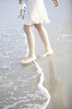 Sahilde yürüyen elbiseli bir kadın.