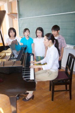 Öğretmen piyano çalarken Asyalı öğrenciler şarkı söylüyor