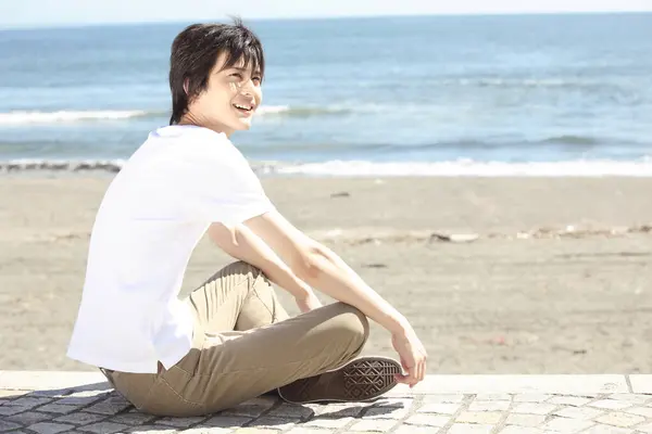 Νεαρός Όμορφος Άντρας Κοντά Μαλλιά Κάθεται Στην Παραλία Στη Θάλασσα — Φωτογραφία Αρχείου