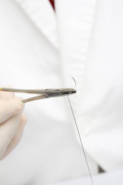 kauçuk eldivenli kadın elleri dikiş ipliği ile makas tutuyor.