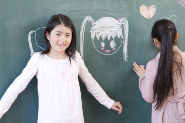 Asyalı kızlar tahtaya tebeşirle resim çiziyorlar. 